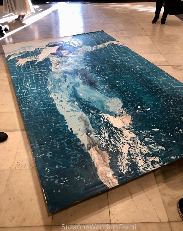 a large painting in blues of a person swimming displayed on the floor in Bikaner House, Delhi