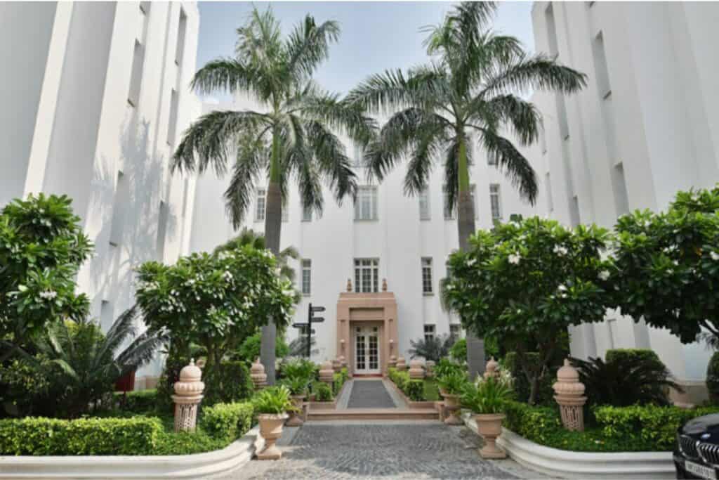 My favourite Connaught Place Delhi home is the Imperial - this is an exterior view of with door and walkway flanked by palm trees and flowering shrubs