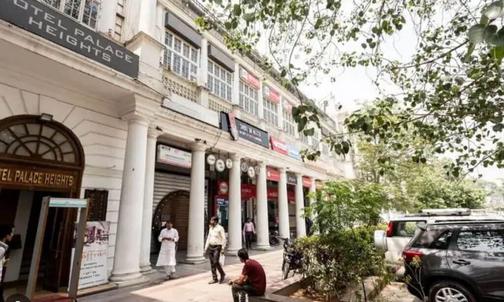 exterior view of white colonnaded Hotel Palace Heights hotel in Connaught Place, Delhi with Indian people walking in futon