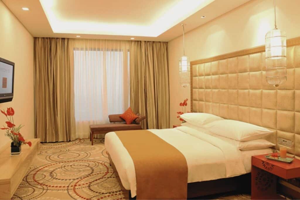 Guest room at the Metropolitan Hotel & Spa, Delhi with large king bed, swirly pattern on carpet and curtains drawn