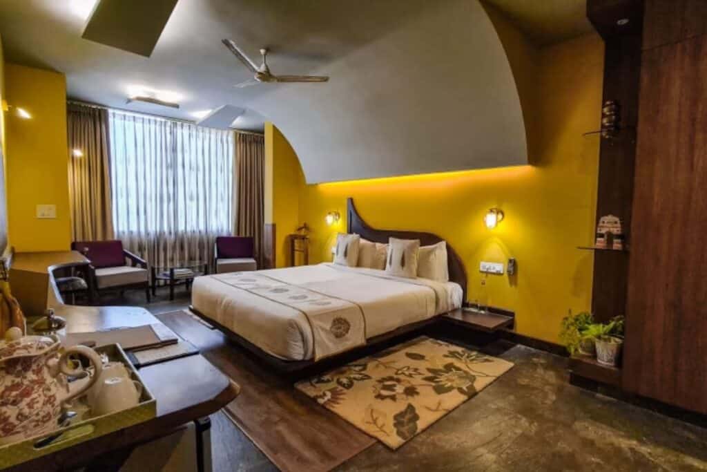 large guest room with yellow accent wall and king size bed, wooden floors at Ekaa Villa in Agra