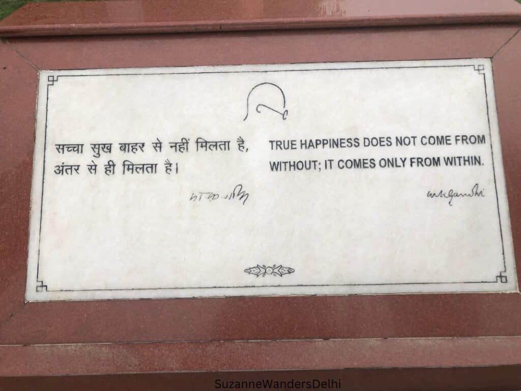 a white marble plaque on red sandstone that reads: True happiness does not come from without; it comes only from within.  This is quote of Gandhi.