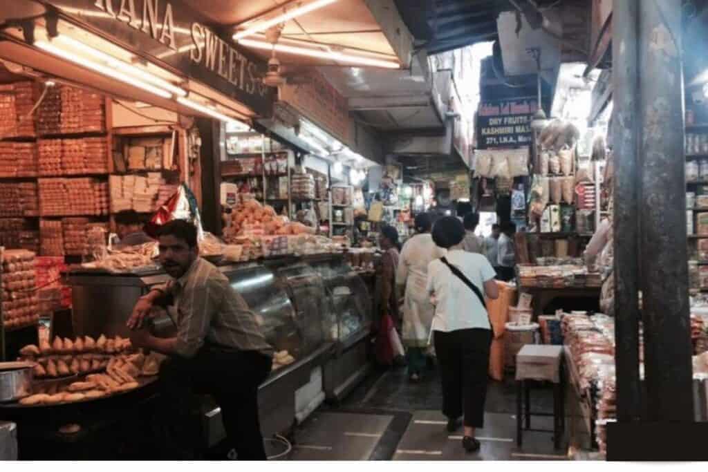 A busy lane in INA Market with Kana Sweets shop on the left and people walking in the lane