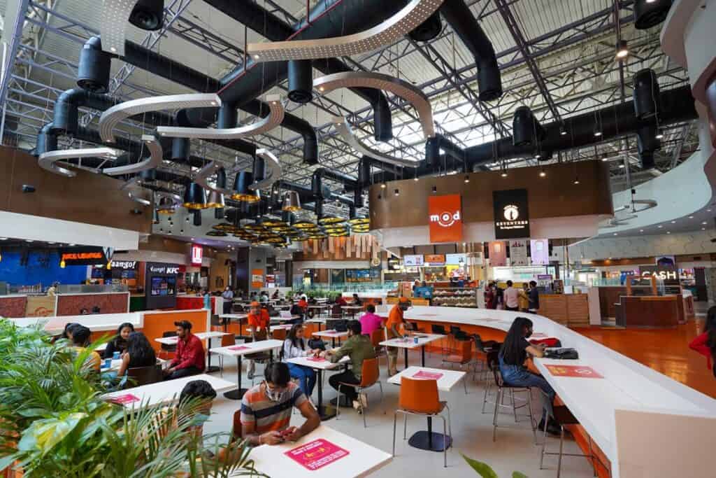 Food court of DLF Mall of India, the biggest shopping malls in Delhi - with explosed artistic piping on ceiling and white tables with orange chairs