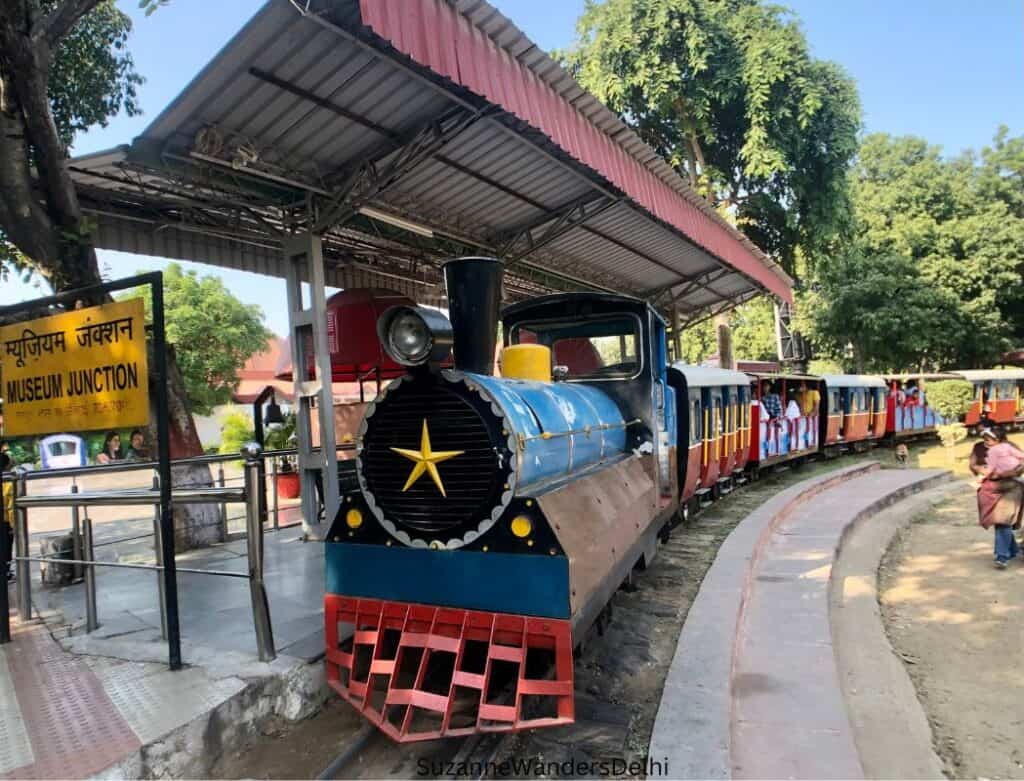 the blue and red Joy Train at pulled up at the Delhi rail museum train station with passengers on board