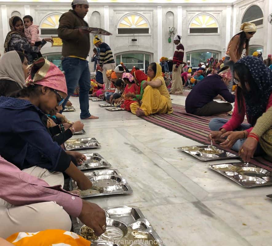 people sitting on the floor of the dining hall in Sri Gurudwara Bangla Sahib while volunteers serve food
