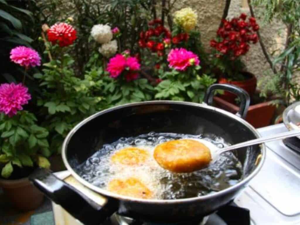 An Indian pot with three potato patties being fried in front of fresh flowers during a cooking class outside a home in Delhi