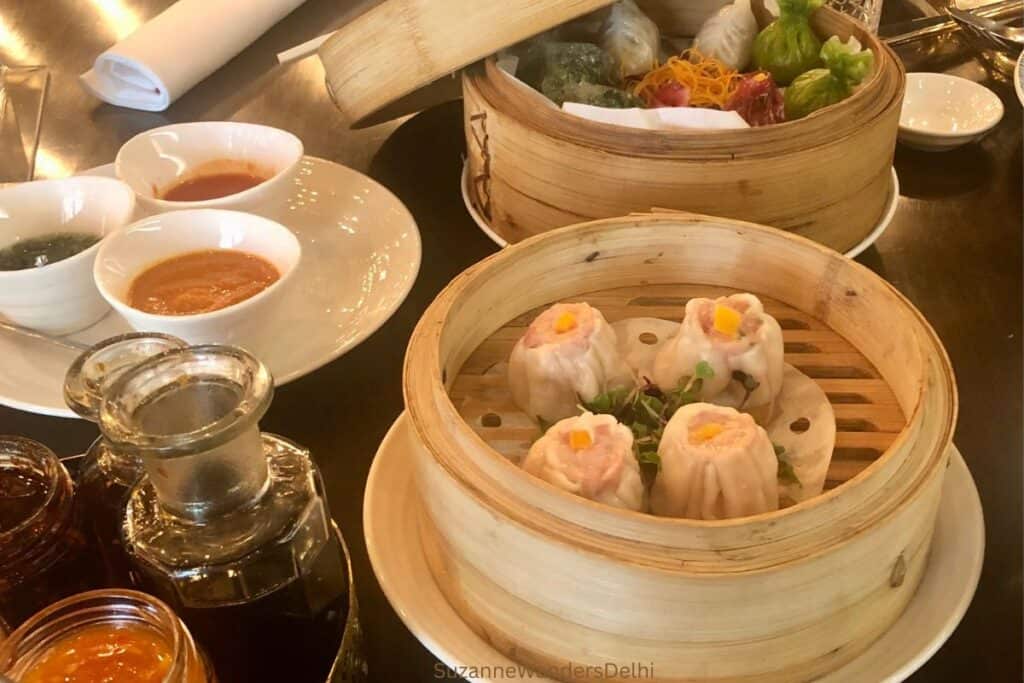 two bamboo steamers full of dim sum and various condiments and sauces on a dark table at Shang Palace in Delhi