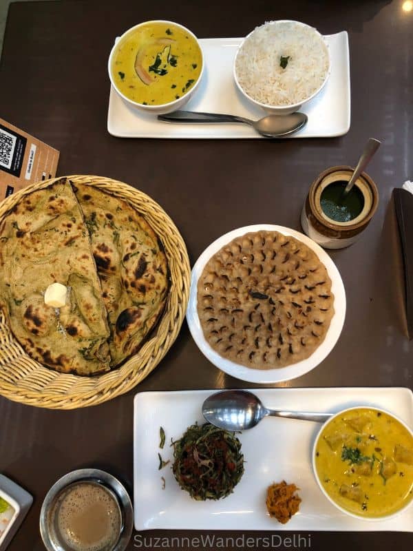 overhead view of two full meals with wicker basket of rotis and metal cups of chai at Lota Cafe, one Delhi's best cafes