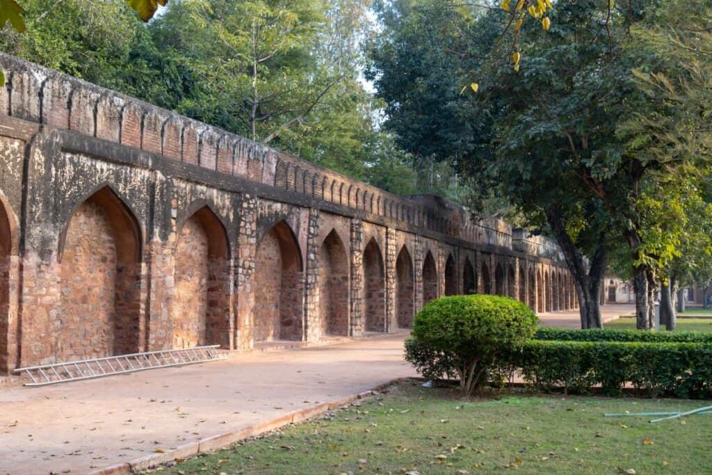 Mughal style stone wall with walking path beside it, green lawns and treest at tomb of Safdarjung