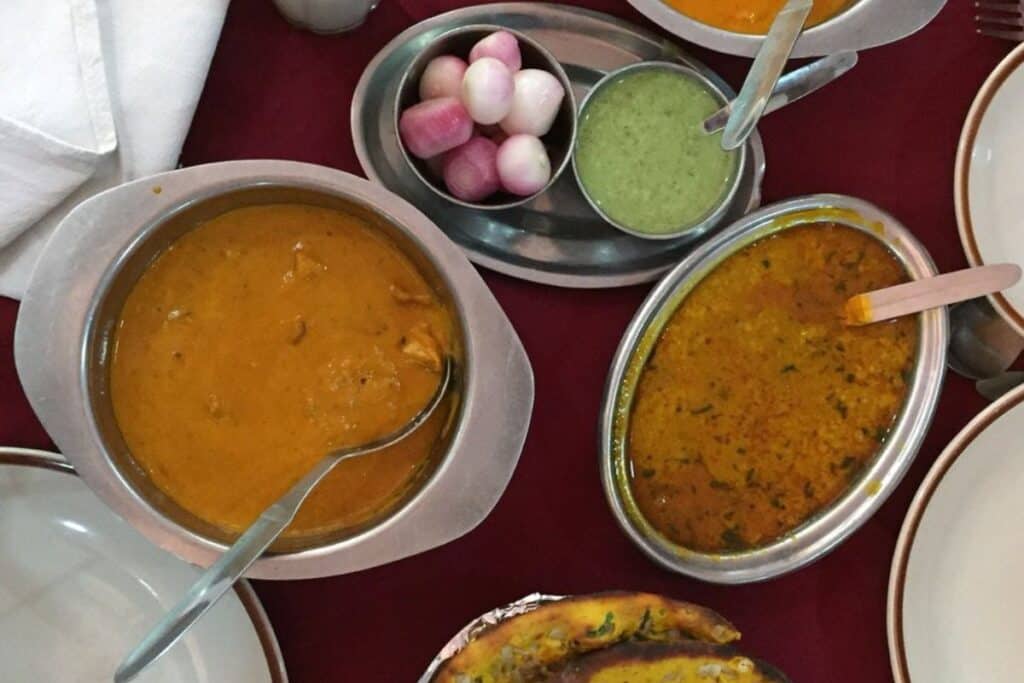 two metal dishes of butter chicken with condiments in metal bowls at Moti Mohal in Old Delhi, a famous restaurant