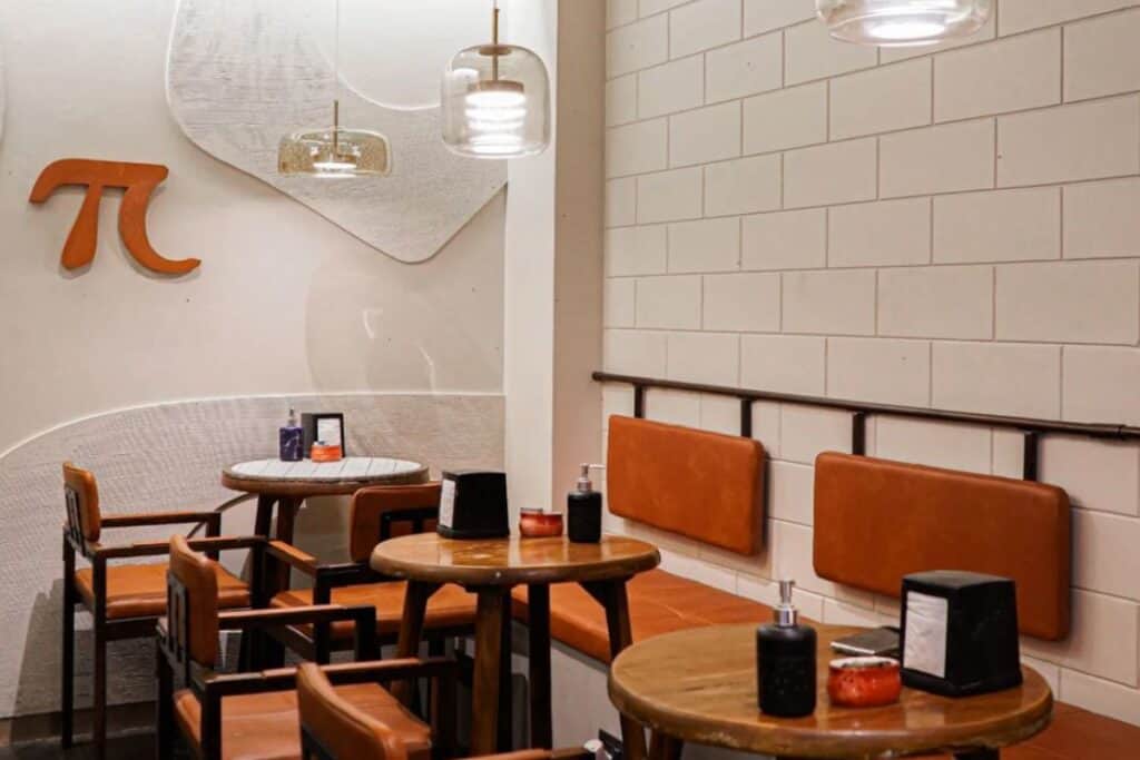 Interior of Tan Coffee shop, with wooden chairs and tables and white brick walls, one of Delhi's best coffee shops