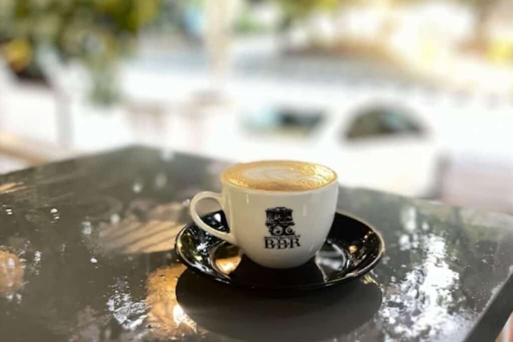 cup of cappuccino in white cup with black saucer and BBR logo, outside on grey table top