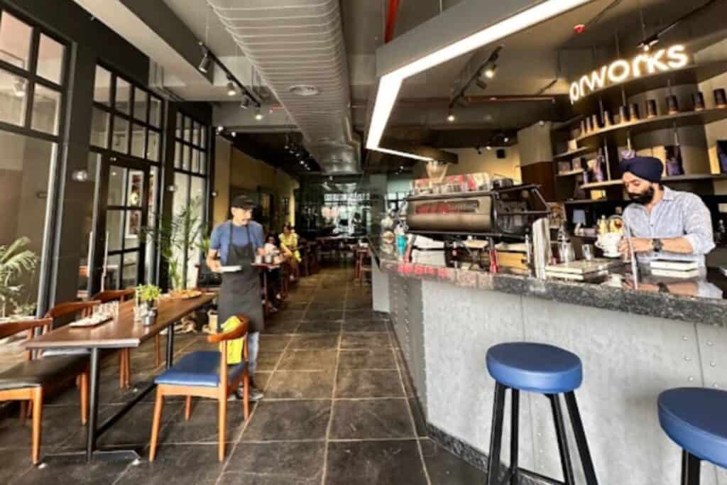 long view of Savorworks (the best artisanal coffee shop in Delhi) coffee shop with man working behind counter and server in background