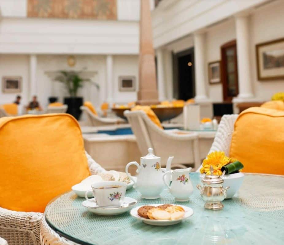 Atrium restaurant in the Imperial Hotel, Delhi showing a round white wicker table with china tea service and orange cushioned wicker chairs