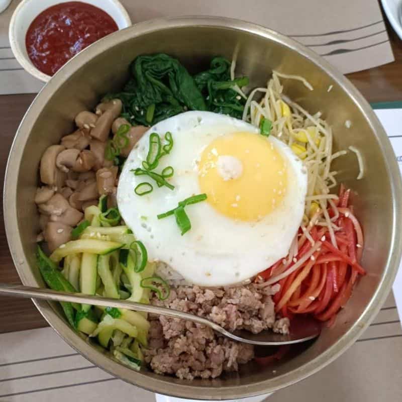 a bowl of bibmap with a sunny side egg on top and a big spoon at the Korean Culture Centre, a good spot for foodies in Delhi