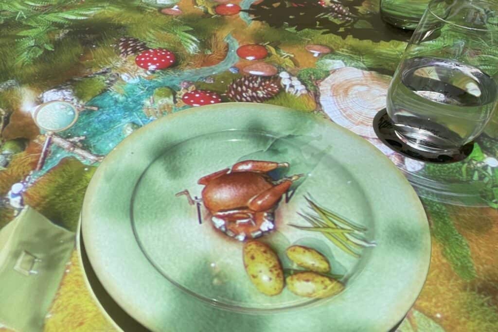 3D images on a dining table and plate showing a whole chicken and potatoes being roasted by a tiny chef, a dining phenomena all foodies will enjoy in Delhi