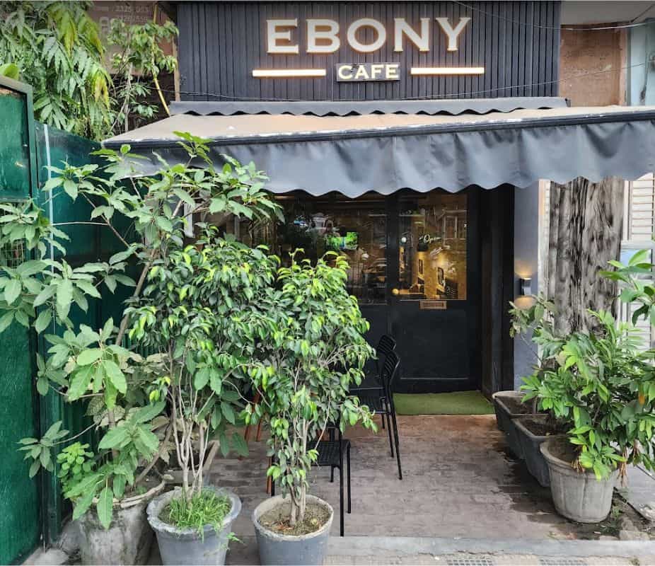 Exterior of Ebony Cafe showing signage and many potted plants around entrance