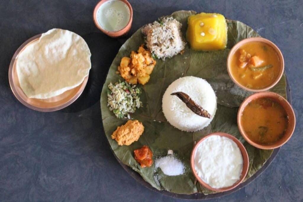 round banana leaf plate with a variety of foods and bowls and with indian food, a clay cup of chai