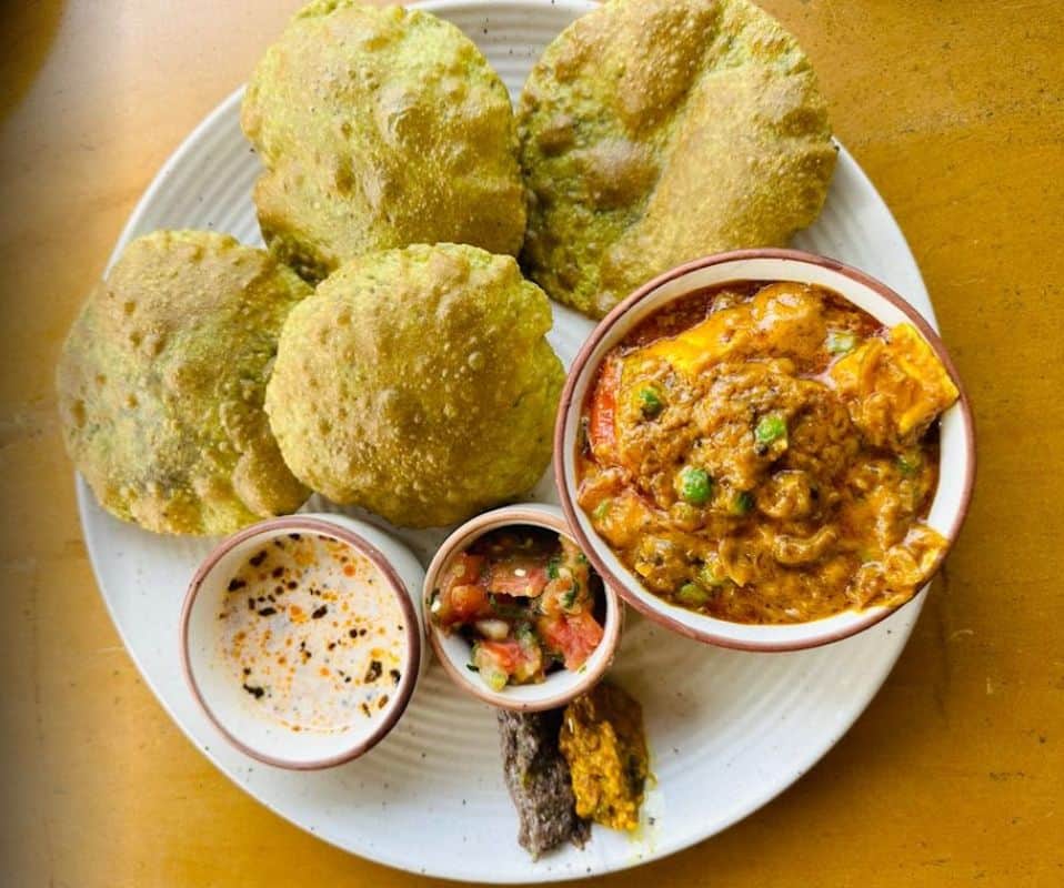 3 small bowls filled with Indian food on a white round plate with 5 puris at Potbelly Rooftop cafe, one of the best cafes in Delhi