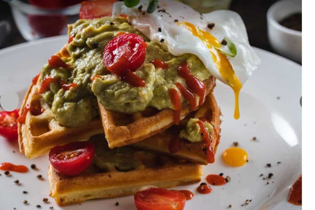 a stack of waffles covered in guacamole and a fried egg at Di Ghent, Delh's best brunch cafe