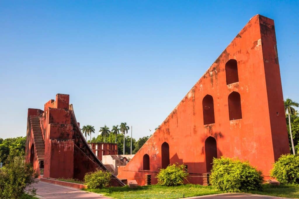 the Shashtansh Yantra set against a bright blue sky with palm trees behind it, at Jantar Mantar in Delhi