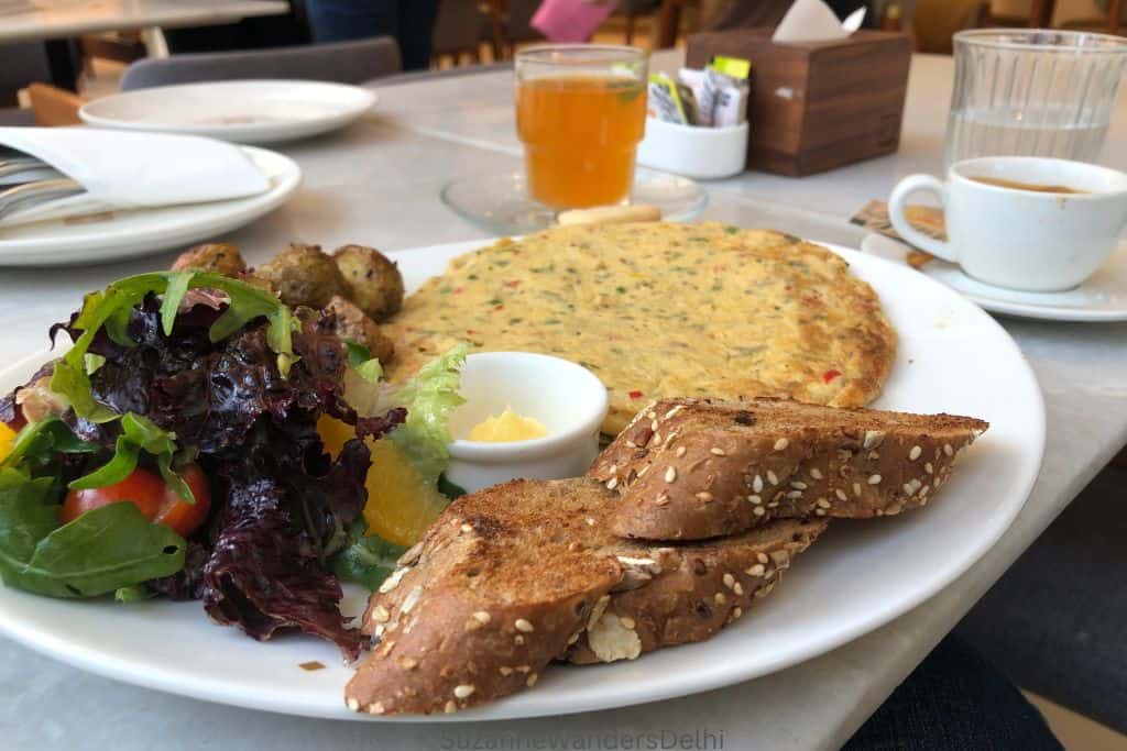 white plate with omelette, bread, salad and tea and coffee in background at Lavonne Cafe in Delhi