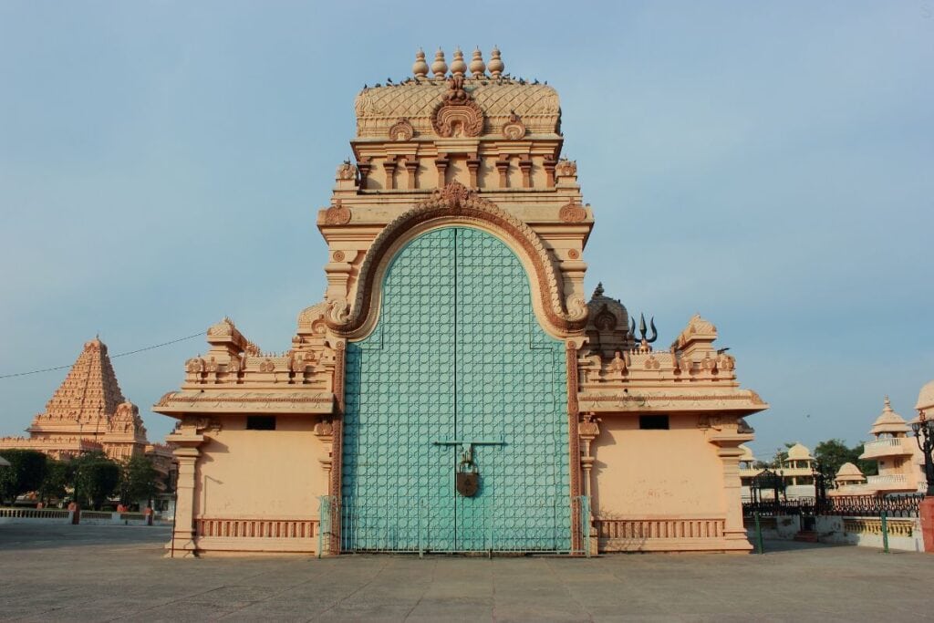 An outdoor elaborately carved stone gate with giant arched blue door and padlock at Chhatarpur Temple in Delhi