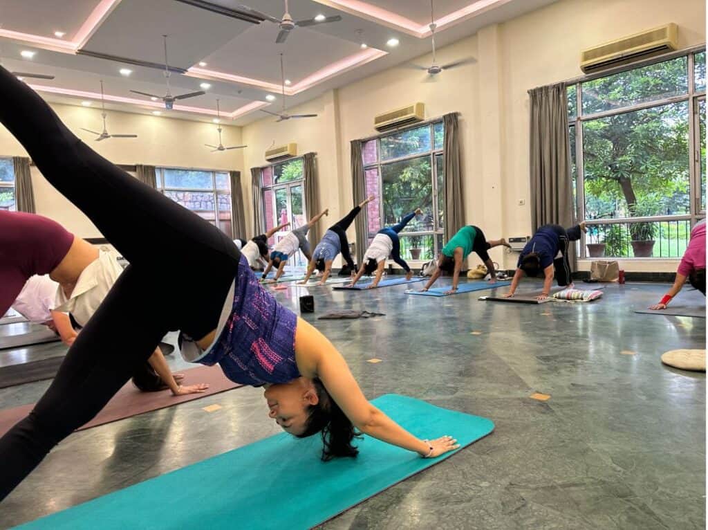 large yoga studio class room with grey marble floor and big windows with students on both sides of room doing downward facing dog pose at P.A. Yoga Studio, one of the best places for yoga classes in Delhi