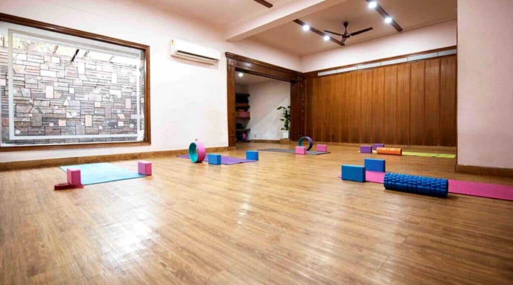 yoga studio with sood floors and big window and a few yoga mats and blocks on the floor at Seema Sondhi The Yoga Studio