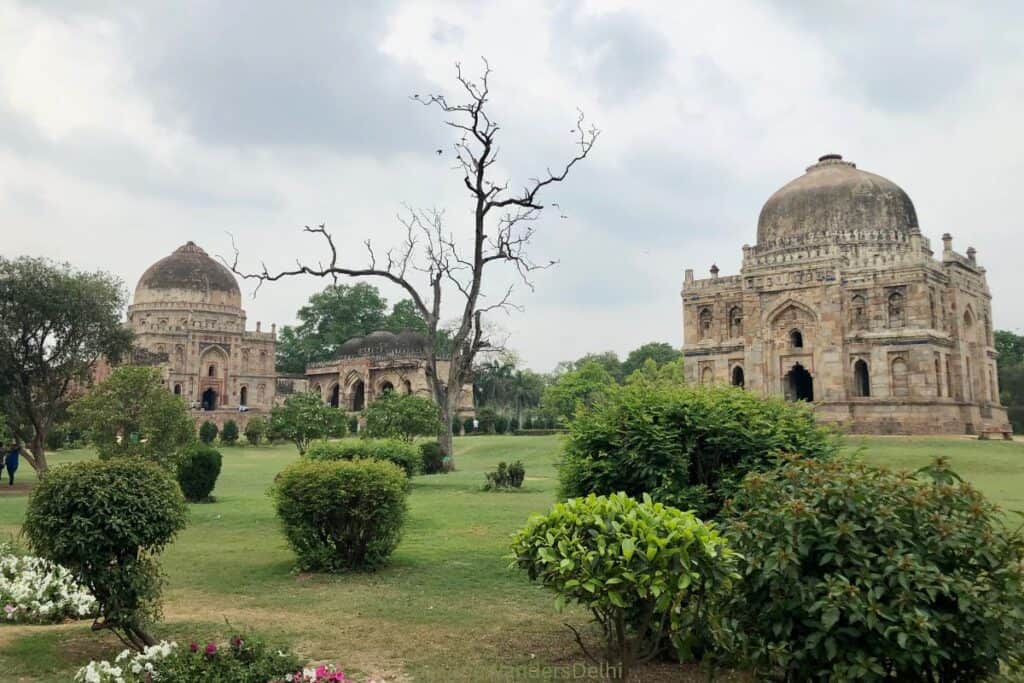 View of 3 tombs in Lodhi Garden with bushes and trees in foreground