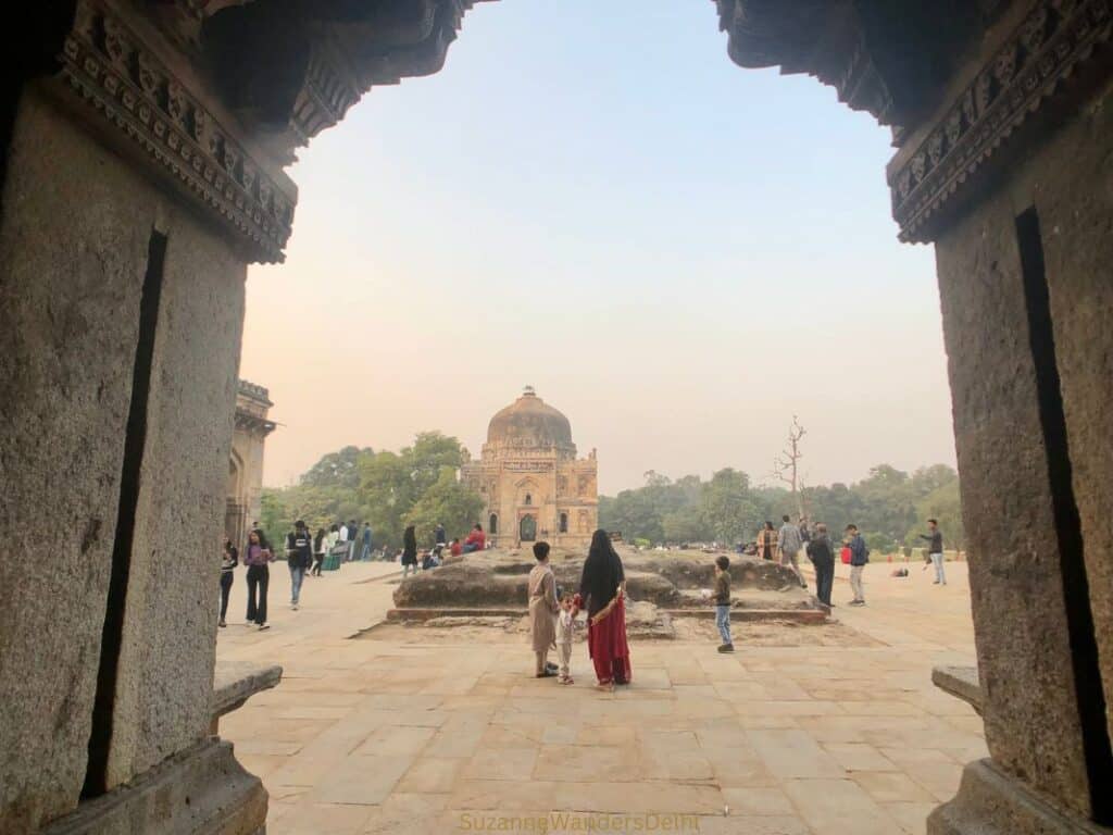 View from inside Bada Gumbad tomb through arched window to other tomb and Indian woman in sari