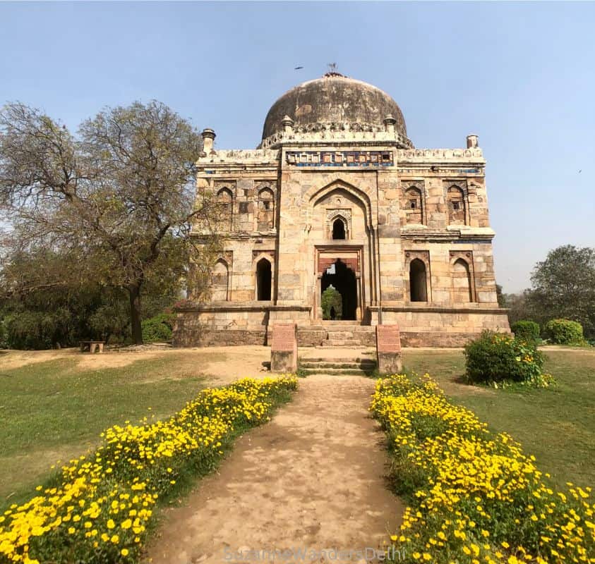 Full view of one of the tombs in Lodhi Garden with domed roof and path lined with yellow flowers leading up to entrance