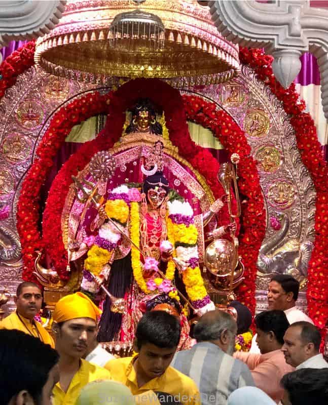 garlanded and dressed deity of Katyayani Devi with crowd of men in front during Navratri