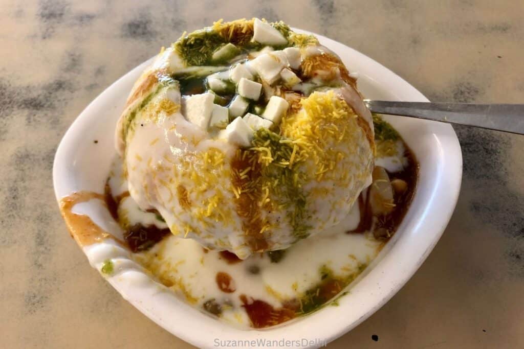 A white plate with raj kachori garnished with paneer cubes, yogurt, tamarind and mint chutneys