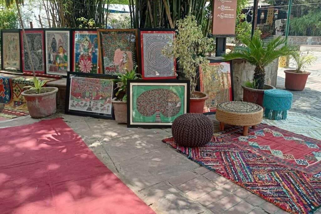 Indian style paintings on display with rugs and colourful stools 