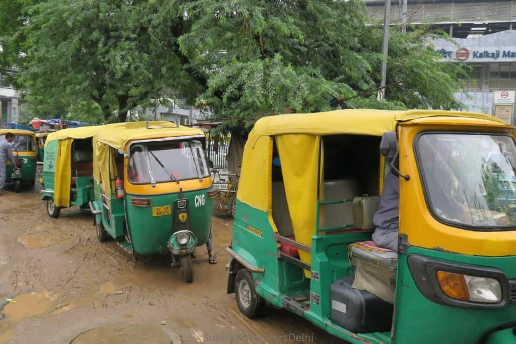 a line up of green and yellow auto rickshaws on a muddy street in Delhi