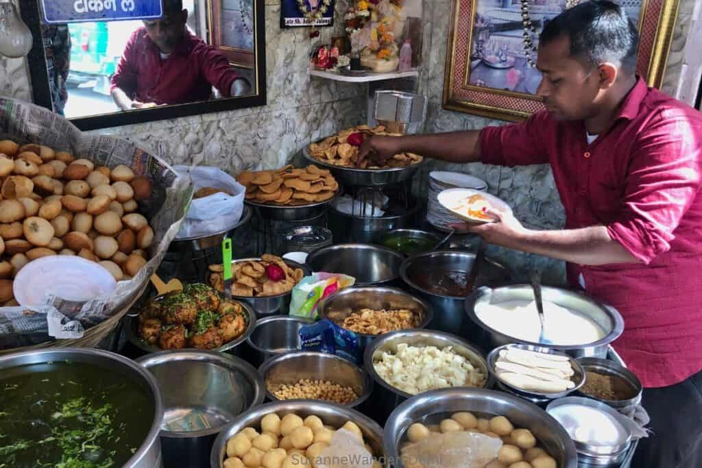 man in red shirt preparing a plate of chaat from a wide selection of items at Ashok Chaat Corner in Delhi