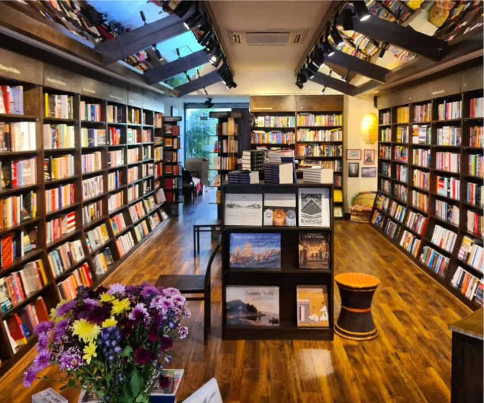 long interior view of the Bookshop Inc, with wooden shelves laden with books and flora arrangement in forefront