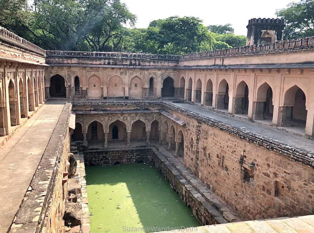 long view of Rajon ki Baoli with green water and three arched levels - you'll see this on Delhi walking tours of Mehrauli