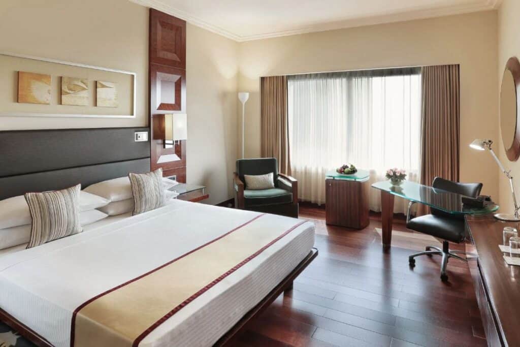 Inside guest room with king size bed in white bedding with beige accents, wooden floors and big window