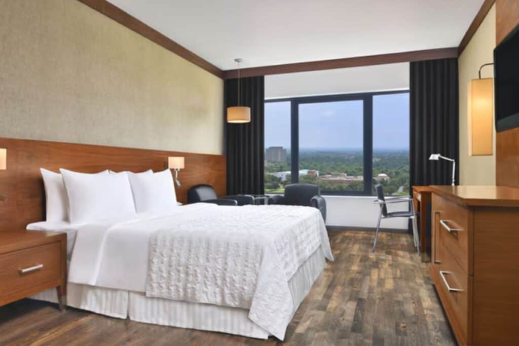 king size bed in white bedding with carpeted room and wood furniture at Le Meridien, one of the best 5 star hotels in Delhi