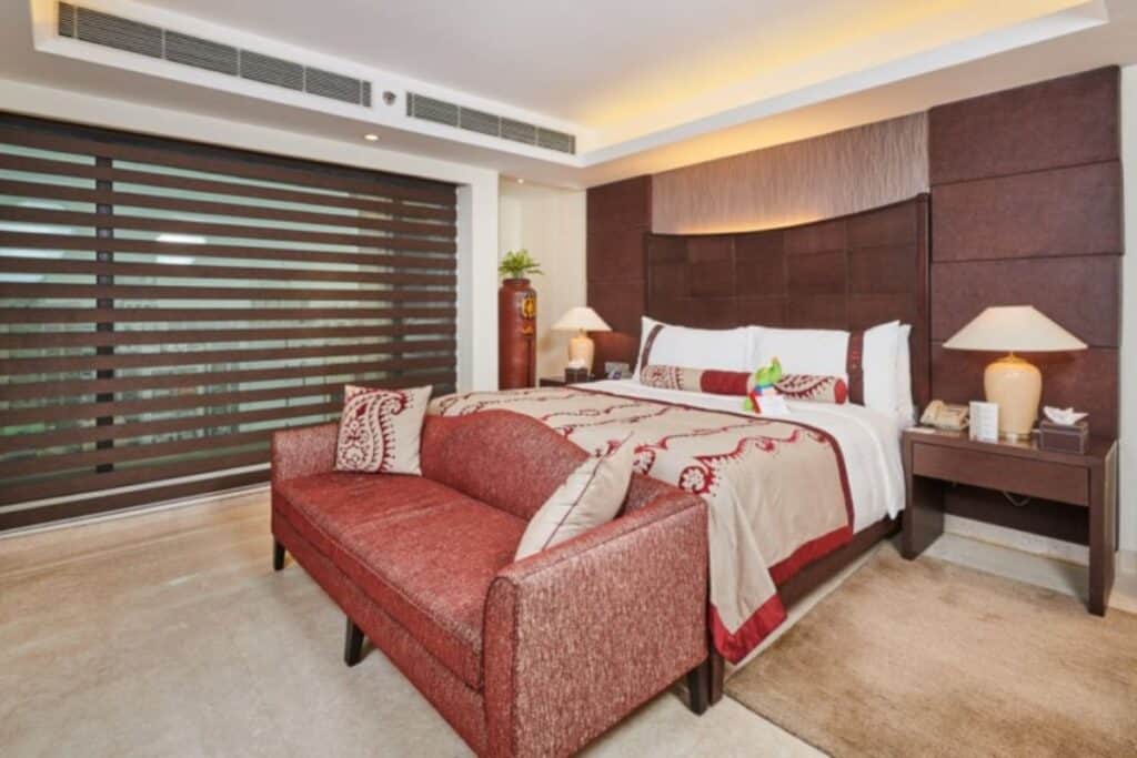 guest room at LaLiT Delhi with king size bed and love seat at foot of bed in orange