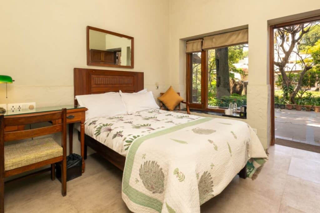 guest room with king size bed and wooden desk, big windows opening to gardens at Lutyens Bungalow in Delhi