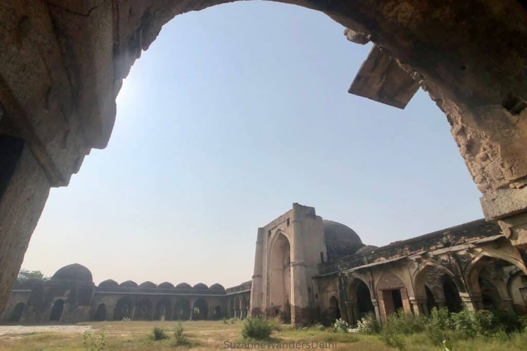 looking through a stone arch at deserted Begampur Mosque, one of the most astonishing places to visit in Delhi