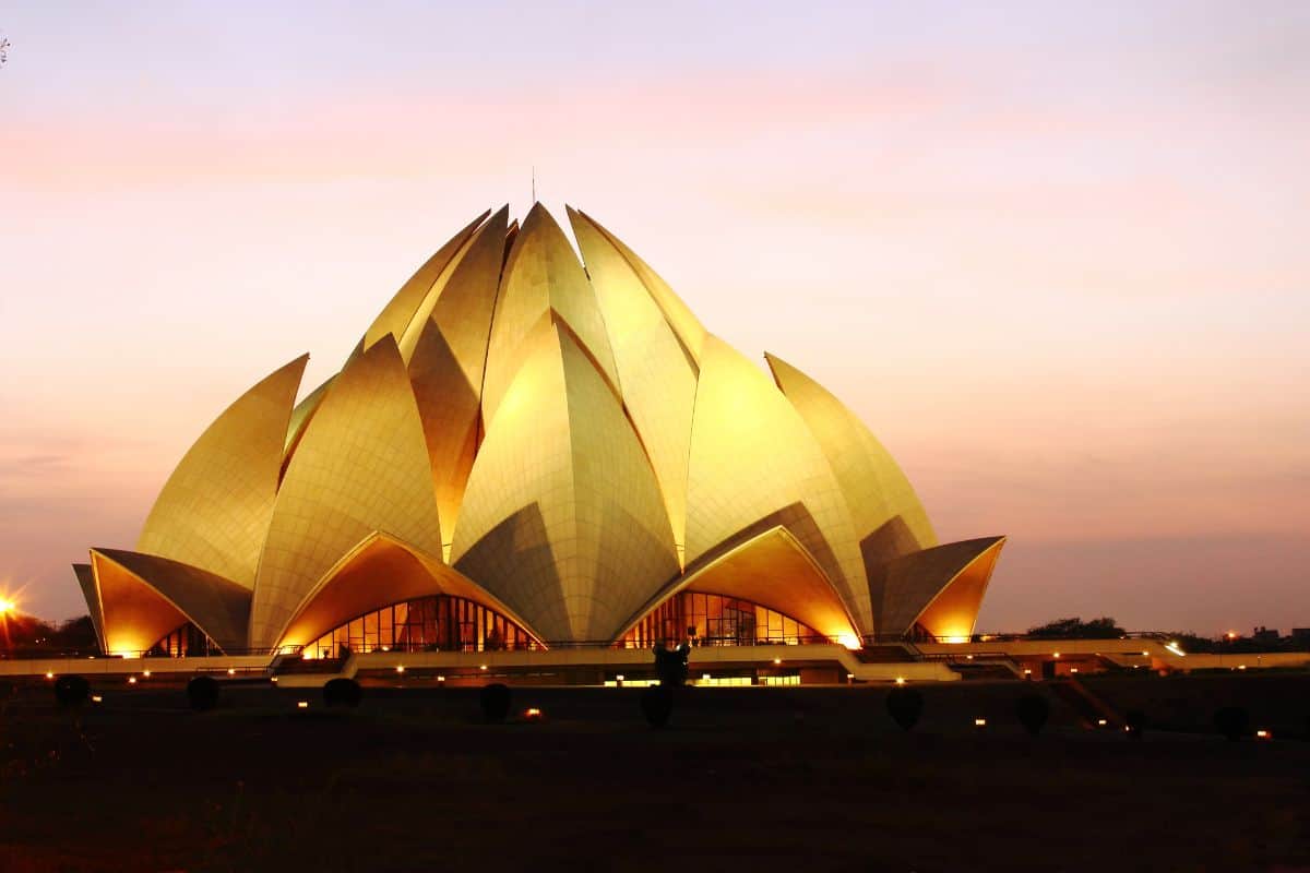 full exterior view of Lotus Temple in Delhi at dusk with pink sky and temple lit up