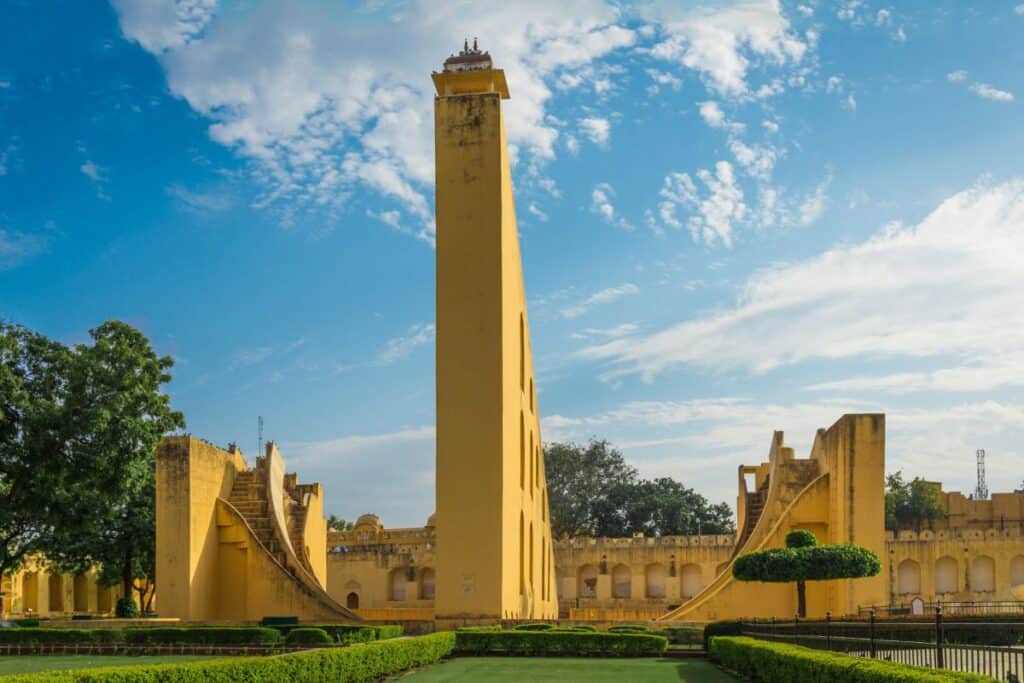 yellow painted Samrat Yantra instrumetn with blue sky and green gardens in Jaipur