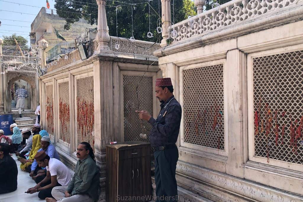 view of marble screen with man standing in front and men sitting on ground at Nizamuddin Basti