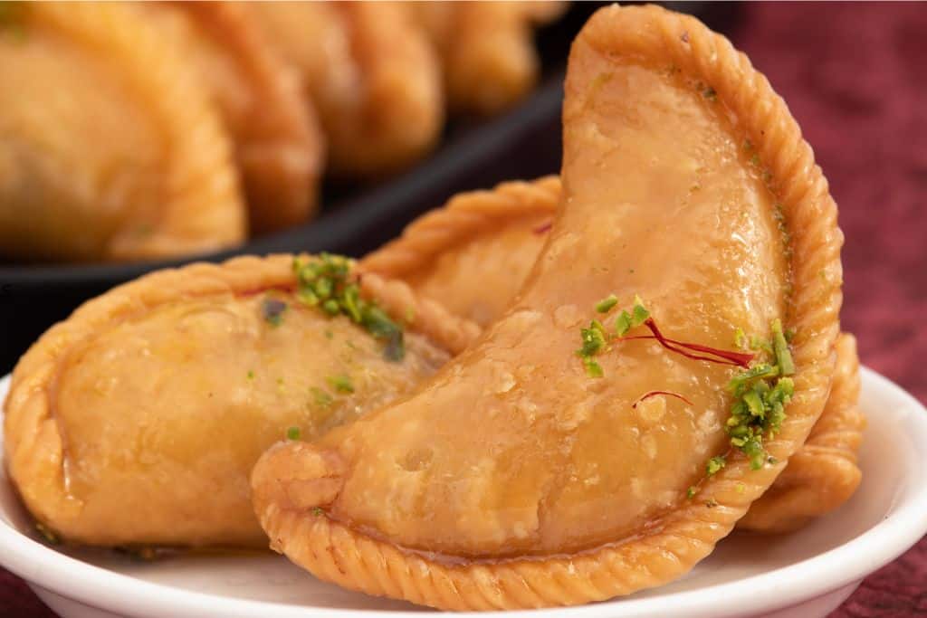 3 gujiya on a plate, a famous sweet eaten in Delhi during Holi