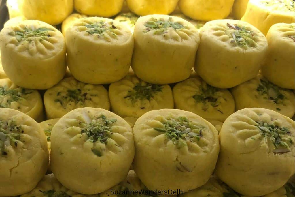 a stack of yellow coloured peda garnished with ground pistachios at Moti Sweets, Delhi